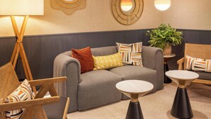A modern lounge area with a grey sofa, patterned cushions, a wooden chair, a small table, and decorative mirrors on the wall.