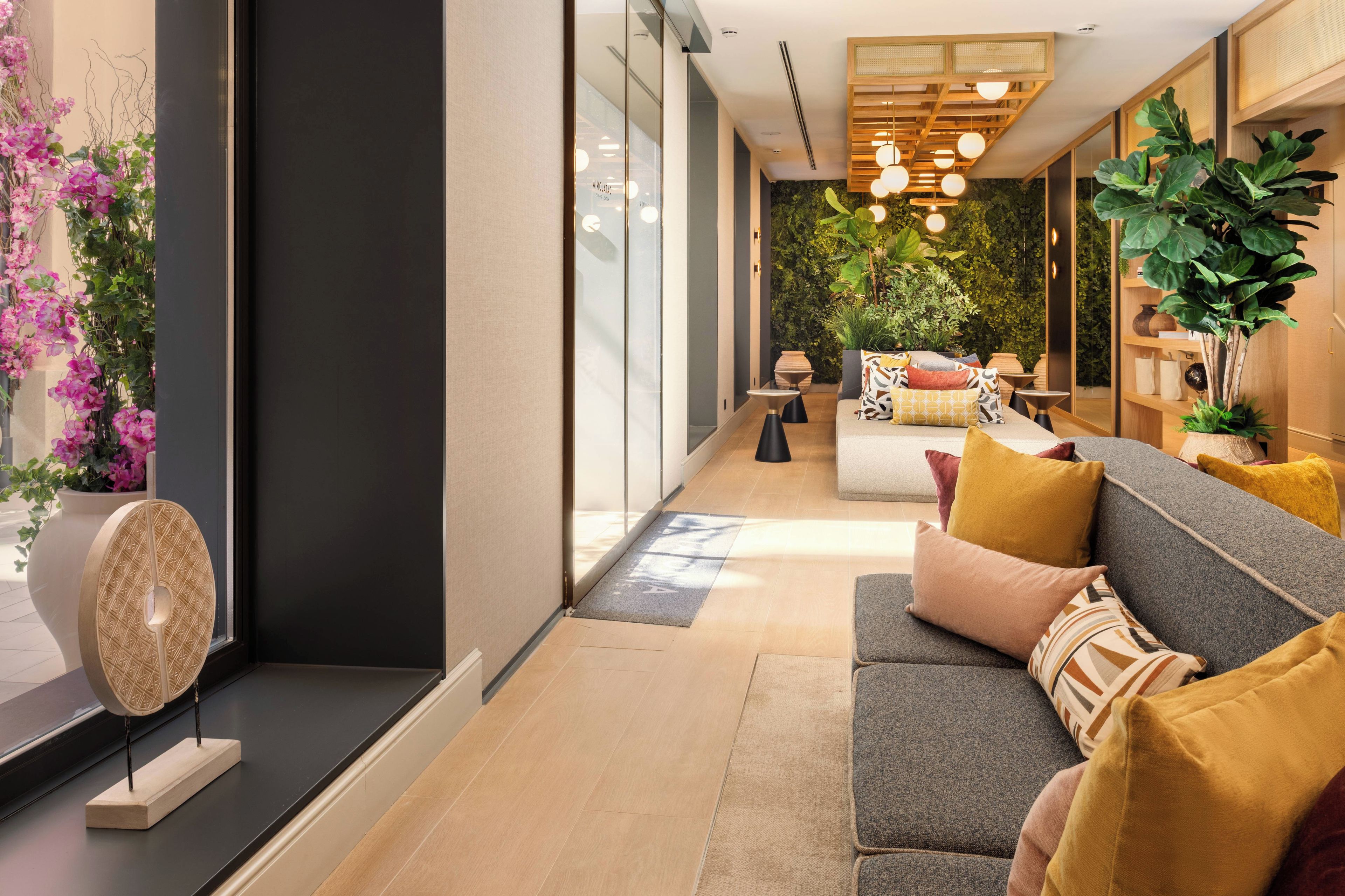 Een moderne woonkamer met een bank, kussens, een salontafel en een decoratieve wand met planten.