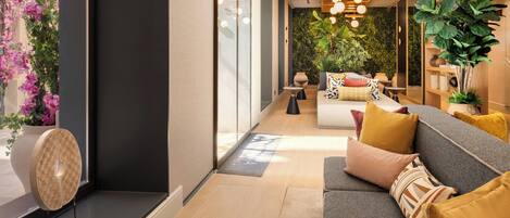 Een moderne woonkamer met een bank, kussens, een salontafel en een decoratieve wand met planten.