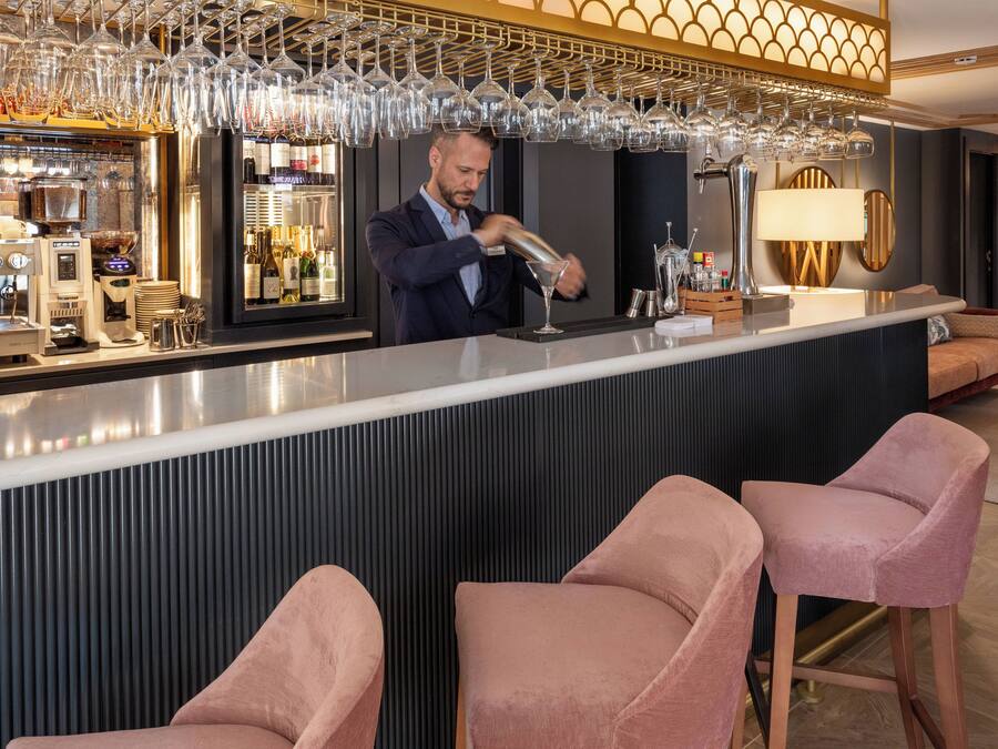 Una zona de bar con un bartender preparando bebidas, un enfriador de vino y taburetes de bar.