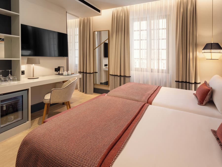 Habitación de hotel con cama, escritorio, silla, televisión y minibar.