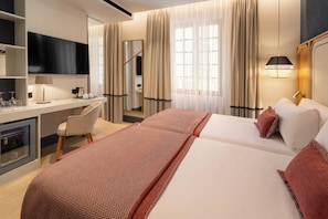 A hotel room with a bed, a desk, a chair, a television, and a minibar. - Catalonia Puerta Del Mar (Málaga)