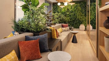Een modern interieur met een bank, kussens, een klein tafeltje en een groene wand met planten.