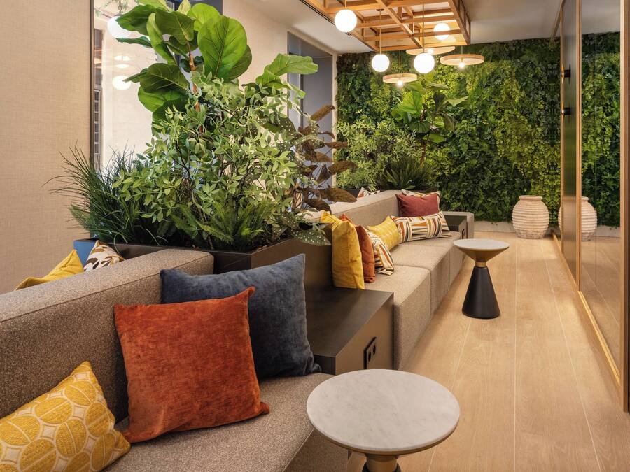 Un interior moderno con un sofá, cojines, una mesita y una pared verde con plantas.