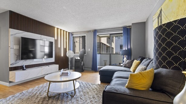 A modern living room with a flat-screen TV, a round coffee table, a sofa with cushions, and a patterned wall. - Modern 2-bedroom next to Stampede +17th w/ Parking (Calgary)