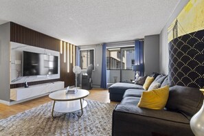 A modern living room with a flat-screen TV, a round coffee table, a sofa with cushions, and a patterned wall. - Modern 2-bedroom next to Stampede +17th w/ Parking (Calgary)
