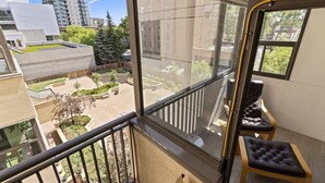 A balcony with a view of a courtyard, a chair, and a window. - Modern 2-bedroom next to Stampede +17th w/ Parking (Calgary)