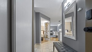 A hallway with a bench, a door, and a room with a bed and desk. - Modern 2-bedroom next to Stampede +17th w/ Parking (Calgary)