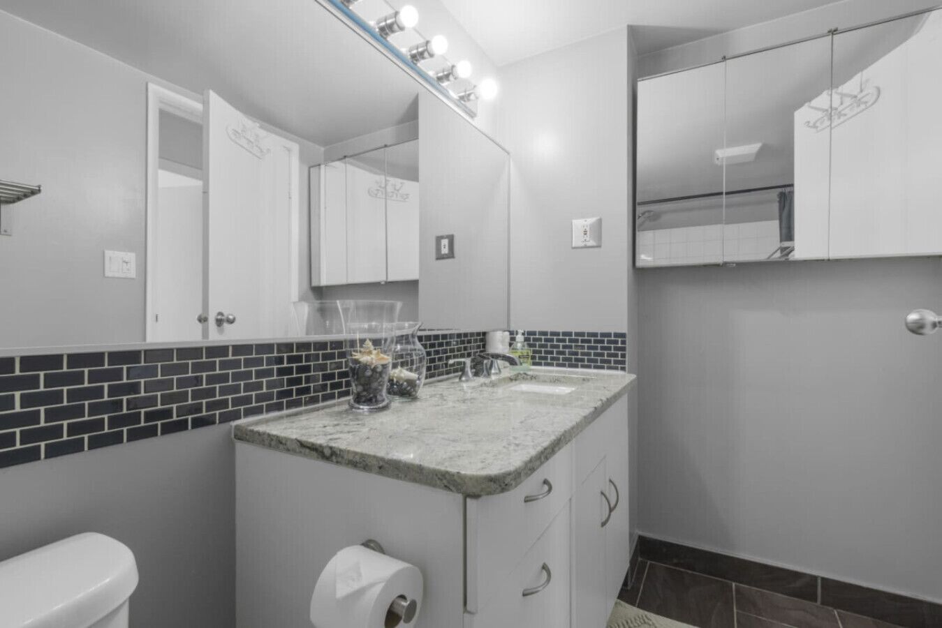 Une salle de bain avec un comptoir en marbre, des toilettes, un miroir et un mur recouvert de carreaux.
