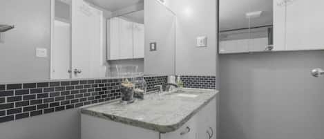 Une salle de bain avec un comptoir en marbre, des toilettes, un miroir et un mur recouvert de carreaux.