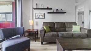 Ein Wohnzimmer mit einer Couch, einem Sessel, einem Tisch und zwei Regalen mit Dekoration.