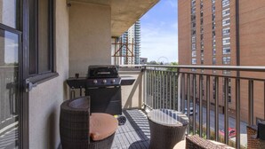 Ein Balkon mit Grill, Korbmöbeln und Blick auf die Stadt.