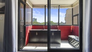 Ein Balkon mit roter Wand, einer schwarzen Bank und Blick auf Gebäude und Bäume.