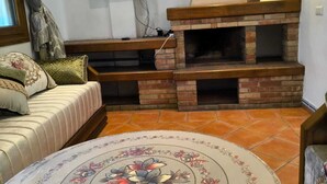 A living room with a brick fireplace, a television mounted on the wall, a sofa with patterned cushions, and a decorative table.