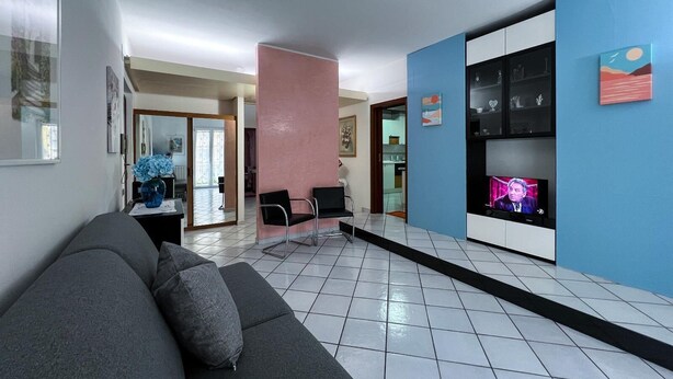 A modern waiting area with a grey sofa, a TV, and a blue accent wall. - Domus Ortensia (Boscoreale)