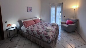 A bedroom with a bed, a chair, a nightstand, and a window with curtains. - Domus Ortensia (Boscoreale)