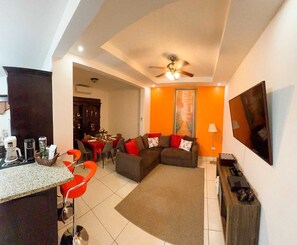 Un espace de vie compact comprenant un coin repas, un ensemble de canapés, un téléviseur et un ventilateur de plafond.