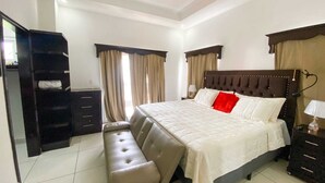 A bedroom with a large bed, a bench, a wardrobe, and a ceiling fan.