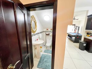 Une vue à travers une porte donnant sur une salle de bain avec un lavabo blanc, des toilettes et un tapis de bain bleu.