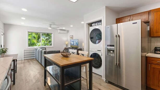 A modern kitchen with a stainless steel refrigerator, a built-in washing machine, and a dining area with a wooden table. - Secluded Forest Retreat Full Kitchen, AC, W/D (Kailua)