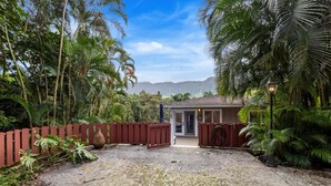 A house with a red gate, surrounded by lush tropical vegetation and a mountain in the background. - Secluded Forest Retreat Full Kitchen, AC, W/D (Kailua)