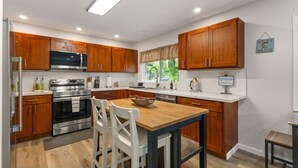 A modern kitchen with wooden cabinets, stainless steel appliances, and a dining area with white chairs. - Secluded Forest Retreat Full Kitchen, AC, W/D (Kailua)