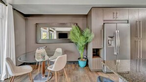 Una cocina moderna con refrigerador incorporado, una zona de comedor con mesa y sillas de vidrio, y una planta en maceta.