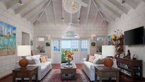 A spacious living room with high ceilings, white walls, and a large window offering a view of the outdoors. There are two white sofas, a wooden coffee table, and a bookshelf with books and decorative items. - Azure Horizon sea view villa (Lower Carlton)