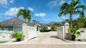 A gated residential area with houses, palm trees, and a clear sky. - Azure Horizon sea view villa (Lower Carlton)