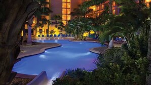 Ein Hotelpoolbereich mit mehreren Schwimmbecken, Palmen und einem Gebäude mit beleuchteten Fenstern.