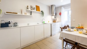 A modern kitchen with white cabinetry, a dining area with a table set for two, and a window providing natural light. - Brisa do Mar in S o Martinho do Porto (Alcobaça)