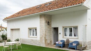 A white building with a tiled roof, a stone pillar, and a small patio with white chairs and a table. - Brisa do Mar in S o Martinho do Porto (Alcobaça)