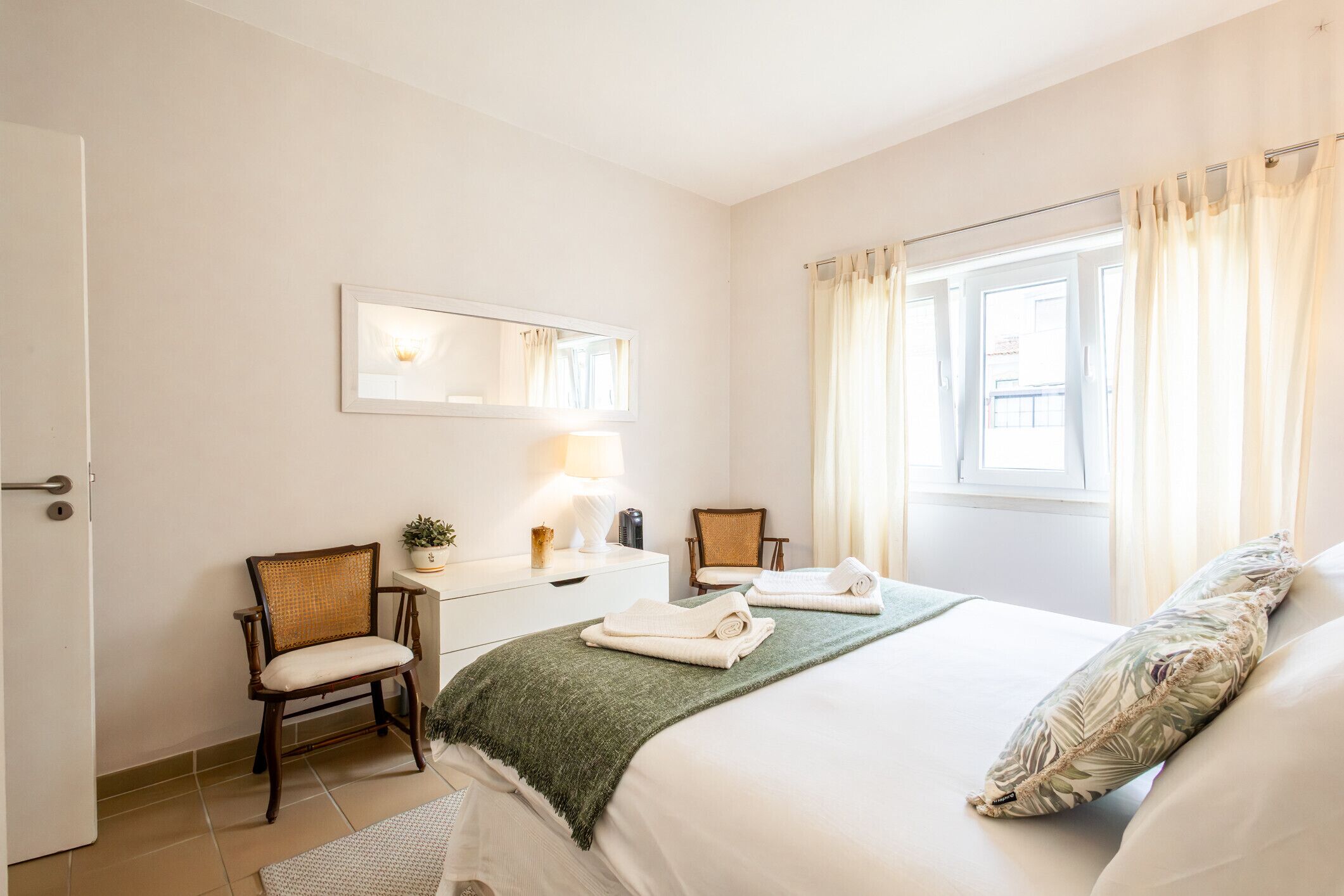 A hotel room with a bed, two chairs, a desk with a lamp, and a window with curtains.