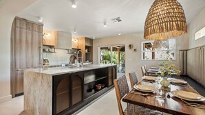 Een moderne keuken met een centraal eiland, houten kasten en een eethoek met een tafel voor vier personen.