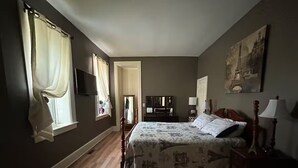 Une chambre à coucher avec un lit, un plancher en bois, une télévision et un tableau accroché au mur.