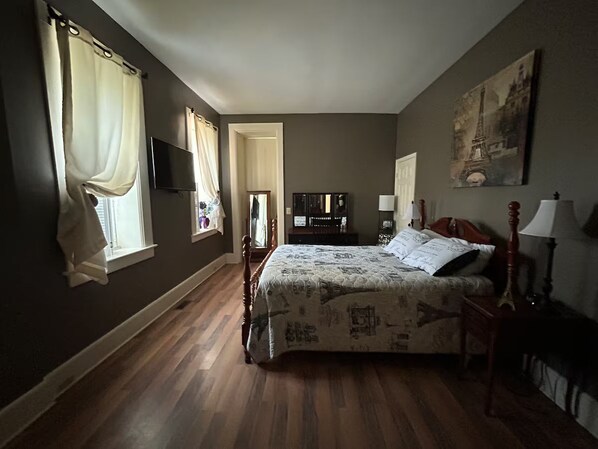 A bedroom with a bed, a wooden floor, a television, and a painting on the wall. - Charming 1-bedroom in Italianate designed house in terrific Albion, NY (Albion)