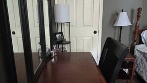 Une longue table à manger en bois, avec des chaises, une lampe et un tableau encadré posé sur une petite table près de la porte.