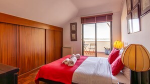 Et hotelværelse med seng, et træskab, en balkon med bord og stole samt et vindue med udsigt.