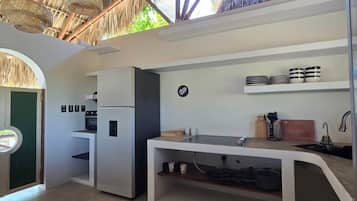 A compact kitchen with a thatched roof, a built-in refrigerator, and a countertop with a sink.