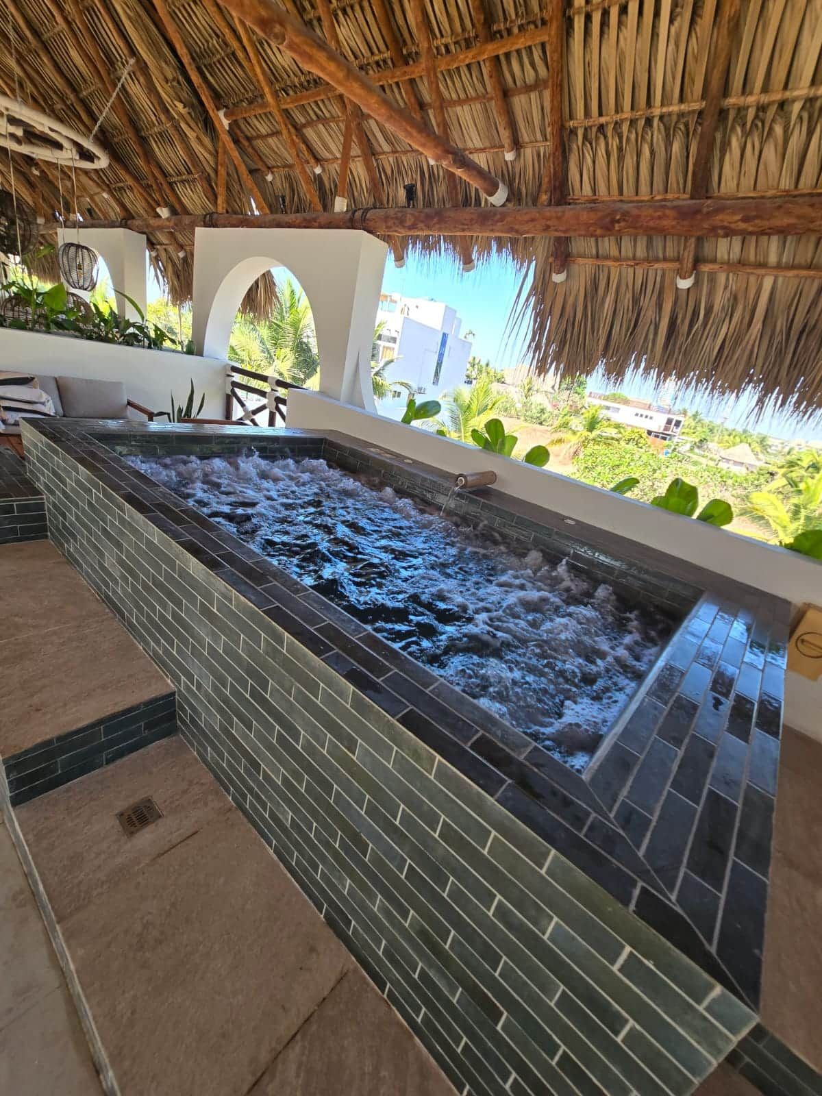 Een wellnessruimte met een jacuzzi, betegelde vloer en rieten dak.