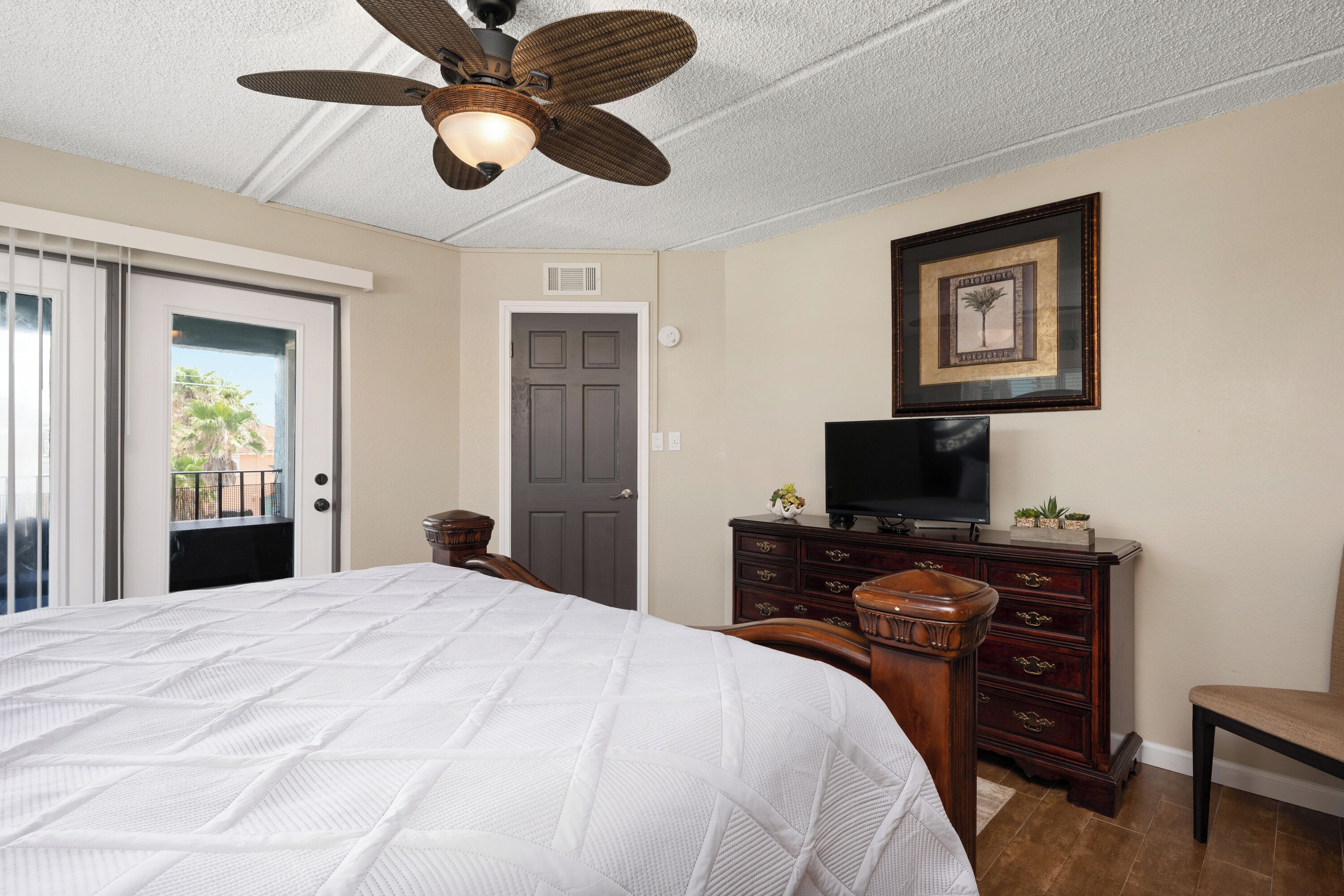 A bedroom with a bed, a dresser, a television, and a ceiling fan.