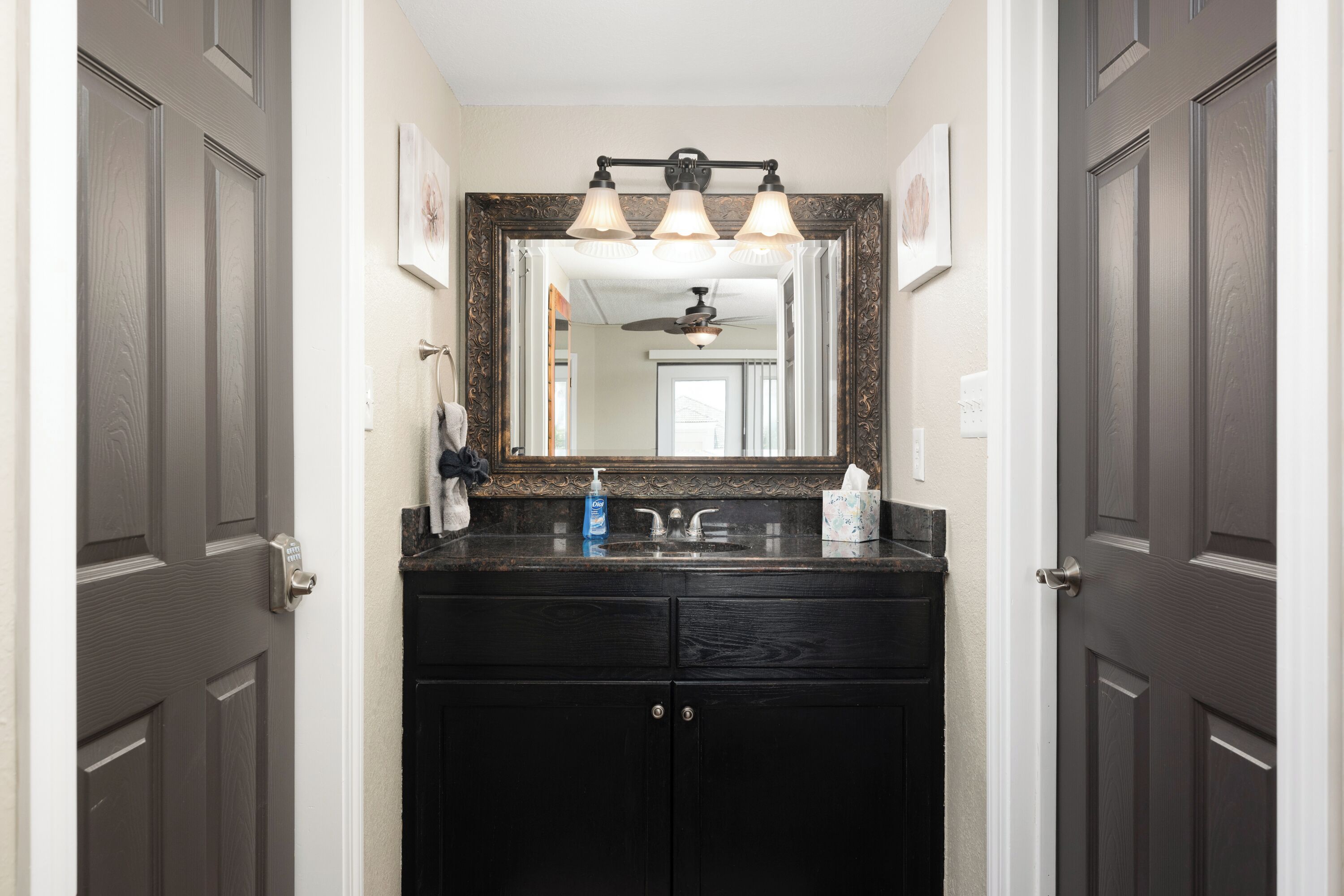 A bathroom with a dark wood vanity, a large mirror, and a ceiling fan.