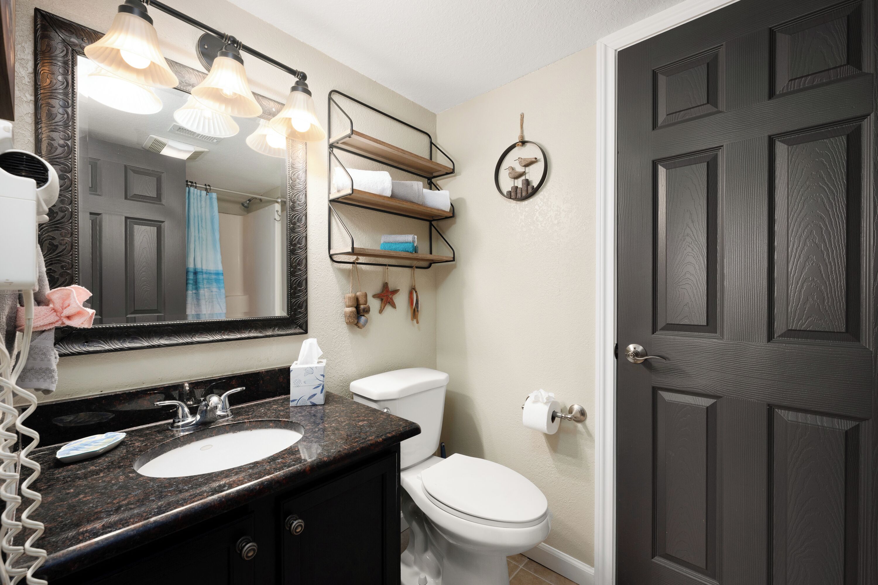 Baño con lavamanos de encimera de granito, inodoro y puerta de madera oscura.