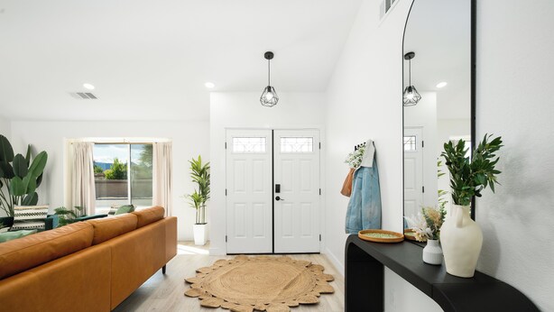 A modern living room with a sofa, a round woven rug, a black console table with a vase and plants, and a large mirror. - NEW! Serene Designer 3BR near Polo & Tennis- SaltPool+Spa, GameRm, Firepit, Golf (Indio)