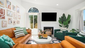 A living room with a fireplace, a large TV, and a green plant. - NEW! Serene Designer 3BR near Polo & Tennis- SaltPool+Spa, GameRm, Firepit, Golf (Indio)