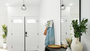 A hallway with a black console table, a large mirror, and a woven rug. - NEW! Serene Designer 3BR near Polo & Tennis- SaltPool+Spa, GameRm, Firepit, Golf (Indio)
