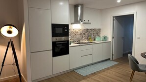 Eine moderne Küche mit weißen Schränken, einem schwarzen Backofen, einer Mikrowelle und einer Edelstahl-Dunstabzugshaube. Es gibt eine geflieste Spritzschutzwand, ein Spülbecken und ein kleines Fenster.