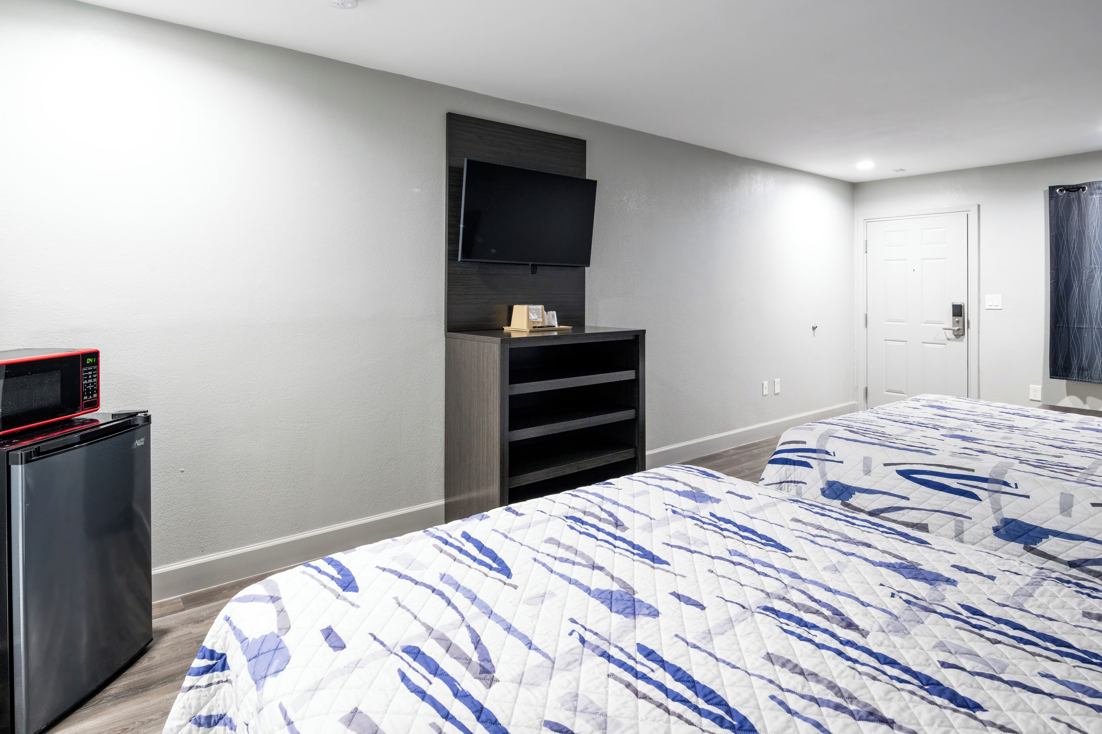 A hotel room with a bed, a TV mounted on the wall, a mini-fridge, and a door with a handle.