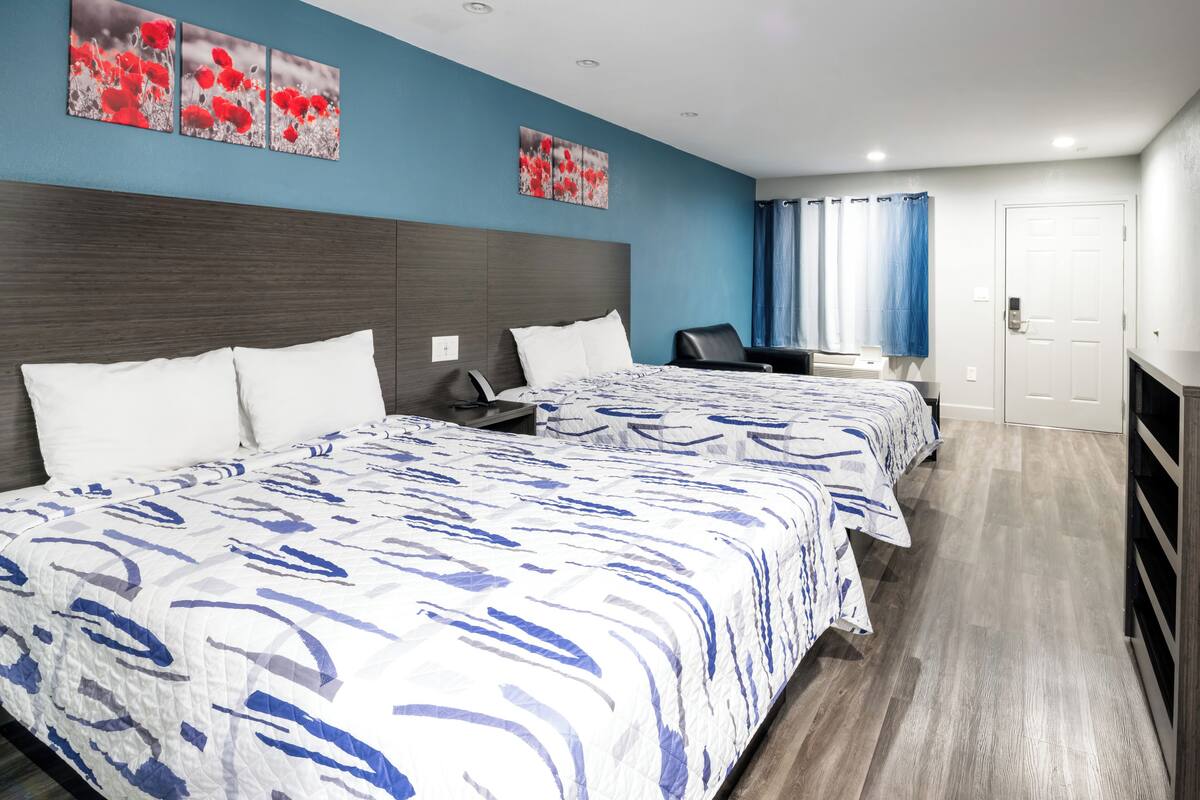 A hotel room with two beds, a desk, a chair, and a door.