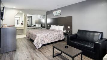 A modern hotel room with a large bed, a black leather sofa, a wooden coffee table, and a flat-screen TV.